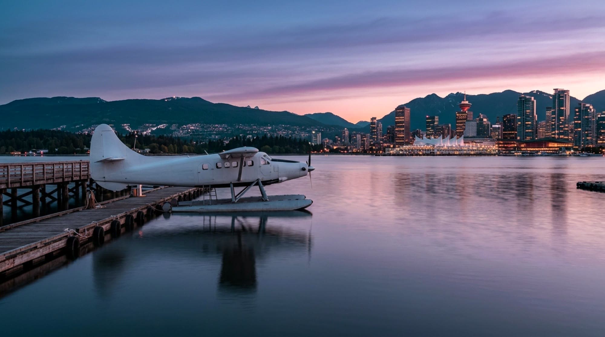 A floatplane at a dock in Vancouver harbour at dawn, the skyline and mountains behind